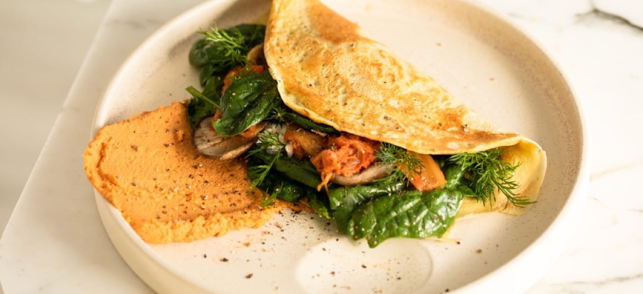 Image of omlette with some green vegetables and tomato on the white plate.